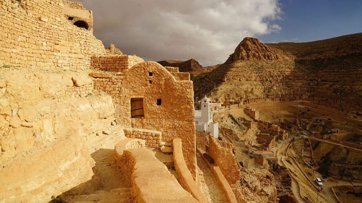 The Berber village of Chenini in Tunisia, with stone houses clinging to the mountainside beneath a cloudy sky.